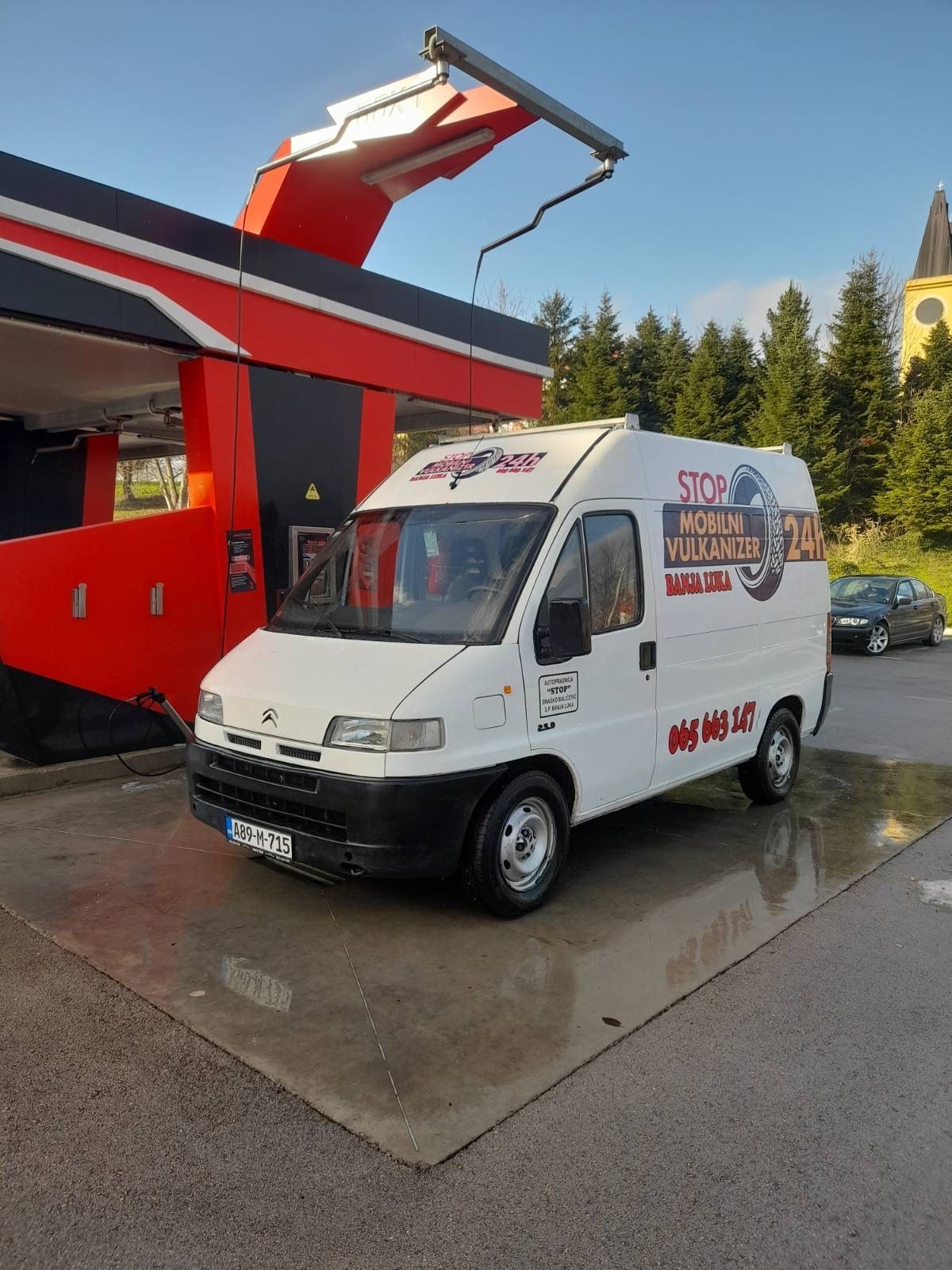 White van with advertisements parked at a car wash station with red and black structure.