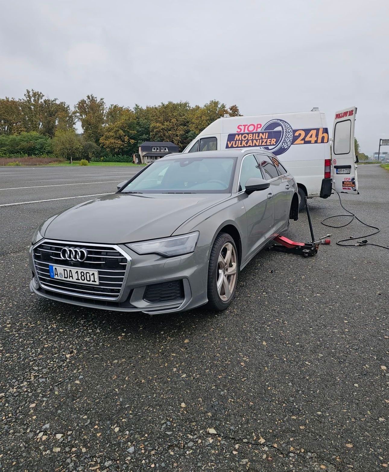 Gray Audi car parked on roadside with a mobile tire service van in the background.